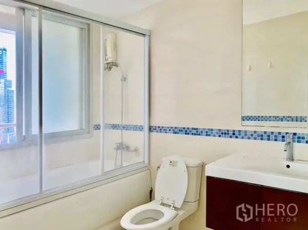 公寓 出租在Bang Rak, Bangkok - 现代浴室，浴缸配玻璃隔断、洗手台与采光窗。