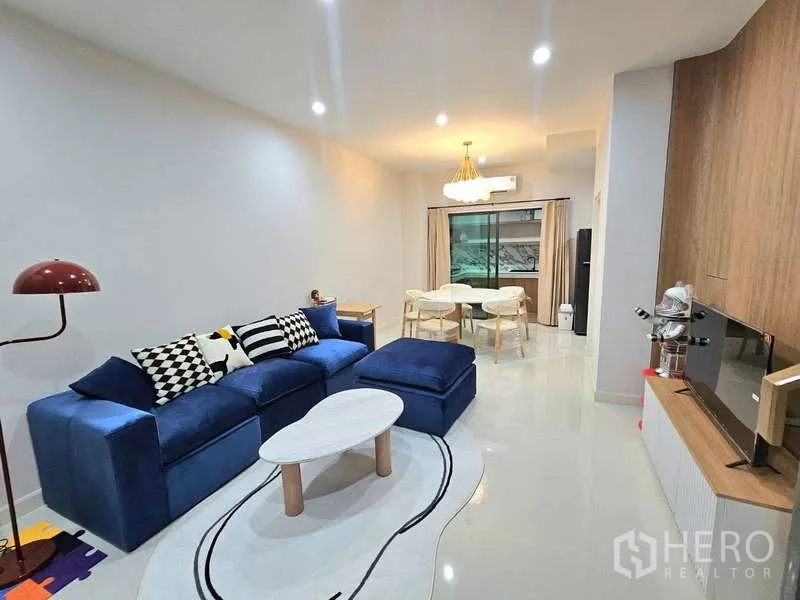 ทาวน์เฮาส์ ให้เช่าในSuan Luang, Bangkok - พื้นที่นั่งเล่นและทานอาหารแบบโอเพ่นแปลน โซฟาสีน้ำเงิน ชั้นวางทีวี และประตูกระจกบานเลื่อน