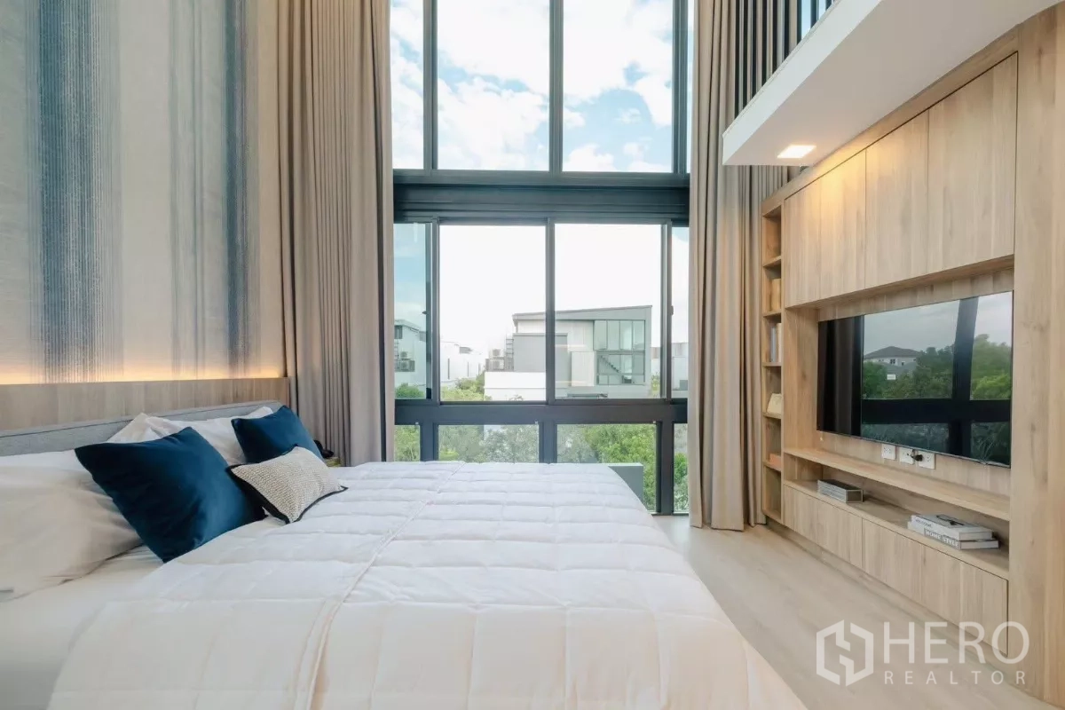Detached House for rent in Saphan Sung, Bangkok - Master bedroom with floor‑to‑ceiling windows, light wood flooring, built‑in TV unit, and neighborhood view.