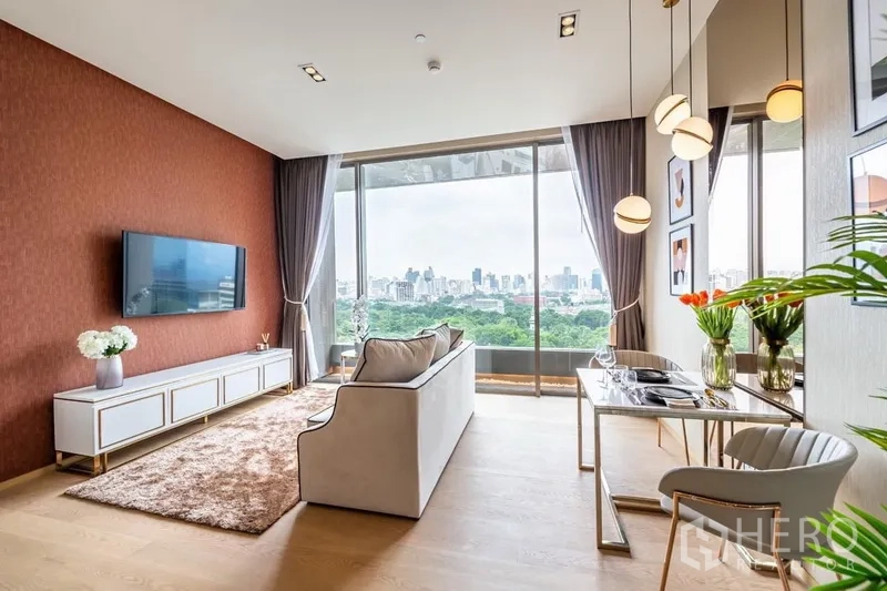 公寓 出租或出售在Bang Rak, Bangkok - 客厅设沙发、壁挂电视与餐桌吊灯，窗外是大片绿意与曼谷天际线。