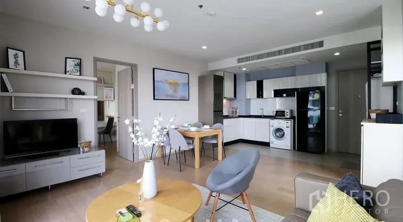 Condominium for rent or sale in Watthana, Bangkok - Open-plan Thonglor condo living room with TV, dining table and U-shaped kitchen with appliances.