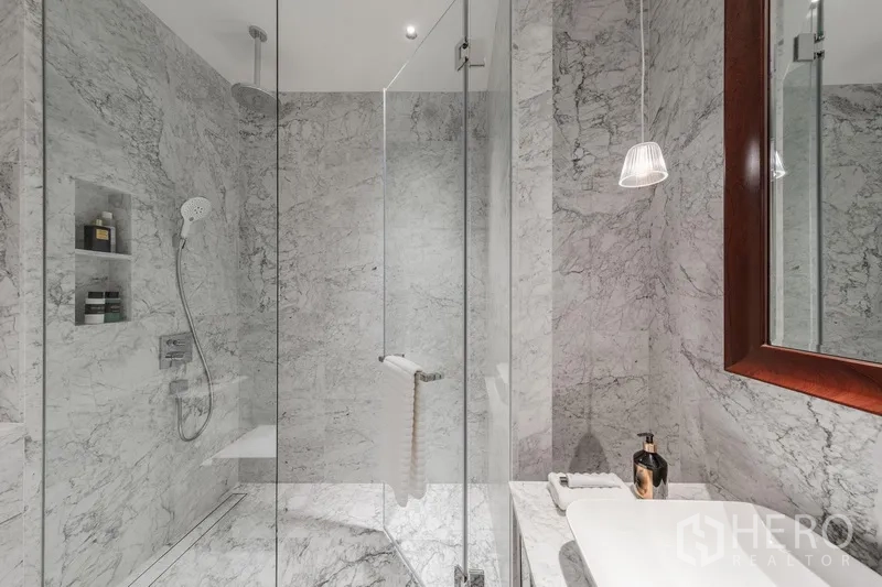 Condominium for sale in Watthana, Bangkok - Marble shower room with glass enclosure, rain shower and vanity with wood‑framed mirror.
