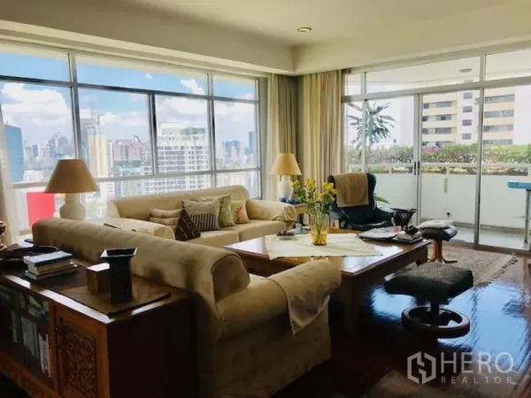 Condominium for rent or sale in Watthana, Bangkok - Corner living room with floor-to-ceiling windows and a city-view balcony.