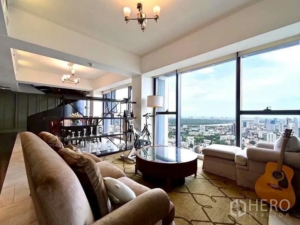 Condominium for rent in Sathon, Bangkok - Cozy lounge with guitar and exercise bike by bay windows capturing river and skyline vistas.