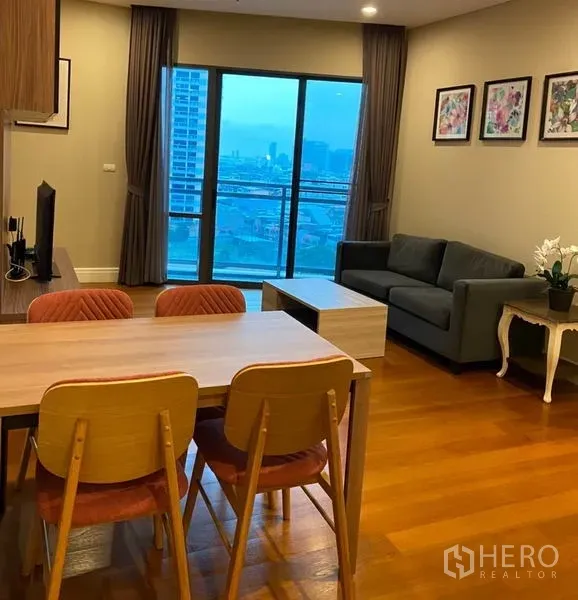 Condominium for rent in Khlong Toei, Bangkok - Open-plan living and dining area with wood floors, sofa, TV and balcony city view.
