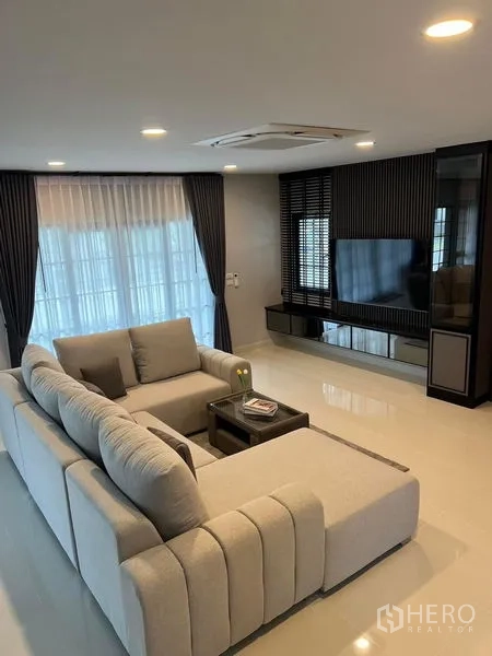 Detached House for rent in Bang Phli, Samut Prakan - Another view of the living zone with sectional sofa facing the TV wall and dark drapes.