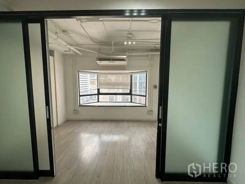 办公空间 出租在Pathum Wan, Bangkok - 推拉磨砂玻璃门后的办公区，裸露天花与宽大的转角窗。