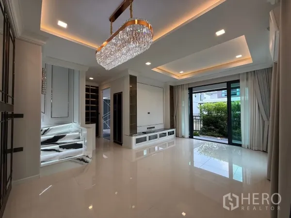 บ้าน ขายในBang Kruai, Nonthaburi - ห้องนั่งเล่นสว่าง เพดานซ่อนไฟ โคมแชนเดอเลียร์ พื้นกระเบื้องเงา และประตูกระจกสไลด์ออกสวน