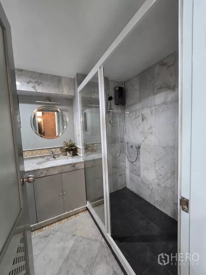 Condominium for rent in Pathum Wan, Bangkok - Bathroom with glass-enclosed shower, marble vanity and round mirror.