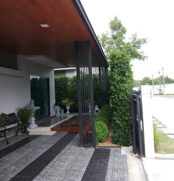 Detached House for sale in Nonthaburi - Front porch under extended roof with vertical metal columns and trimmed shrubs.