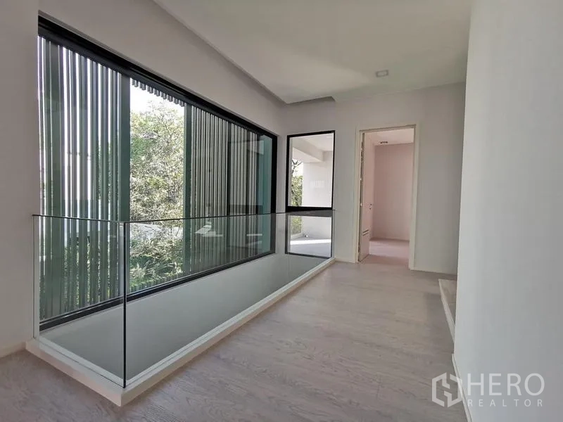 Detached House for rent or sale in Saphan Sung, Bangkok - Bright corridor with glass balustrade and tall windows overlooking greenery.