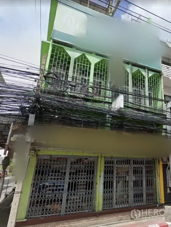 อาคารพาณิชย์ ให้เช่าในHuai Khwang, Bangkok - อาคารพาณิชย์สูงสามชั้นสีเขียวในย่านห้วยขวาง ชั้นล่างประตูเหล็กยืด ชั้นบนมีระเบียงลูกกรง ติดถนนคึกคัก
