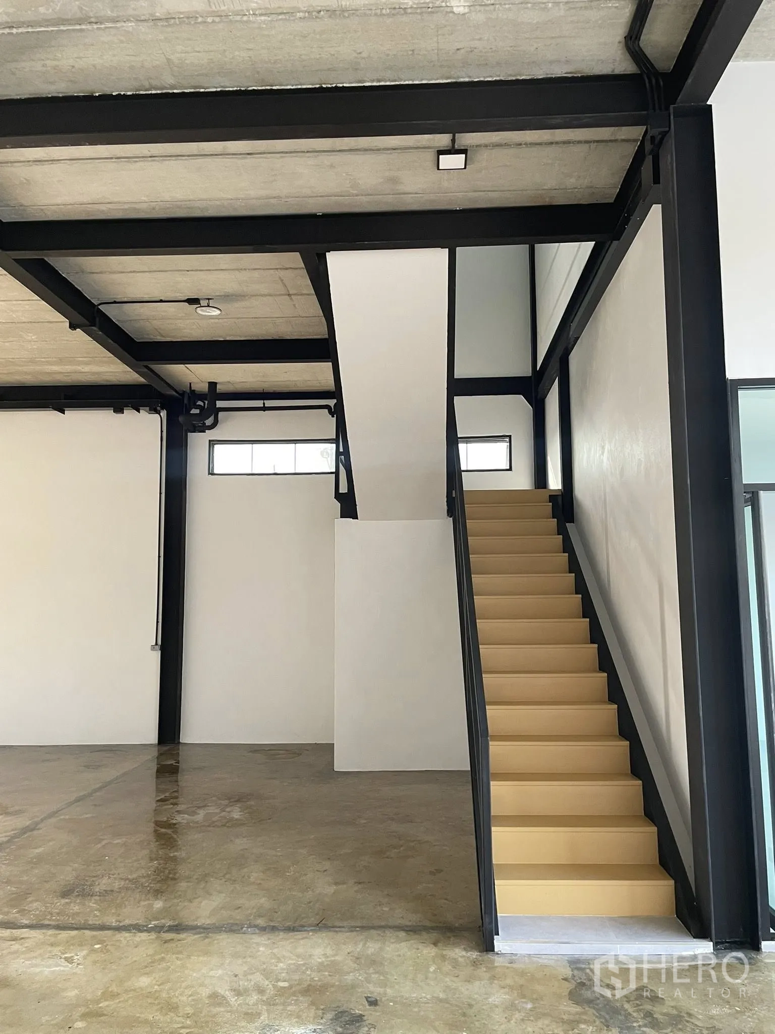 Warehouse for rent in Phra Samut Chedi, Samut Prakan - Ground-floor bay with black steel frame and straight staircase to the mezzanine.