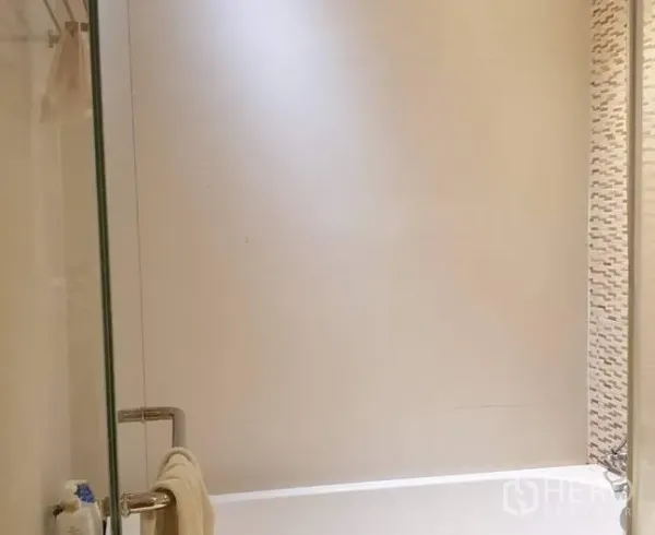 Condominium for sale in Khlong Toei, Bangkok - Bathroom with a glass shower screen and bathtub featuring a tiled accent wall.