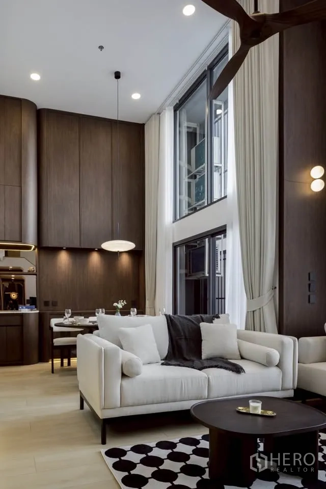 Condominium for rent in Khlong Toei, Bangkok - Spacious lounge featuring a white sofa, coffee table, tall curtains and contemporary lighting.