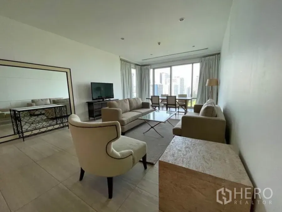 公寓 出租在Pathum Wan, Bangkok - 明亮客厅配米色沙发、玻璃茶几与电视柜，落地窗享城市景观并设用餐区。