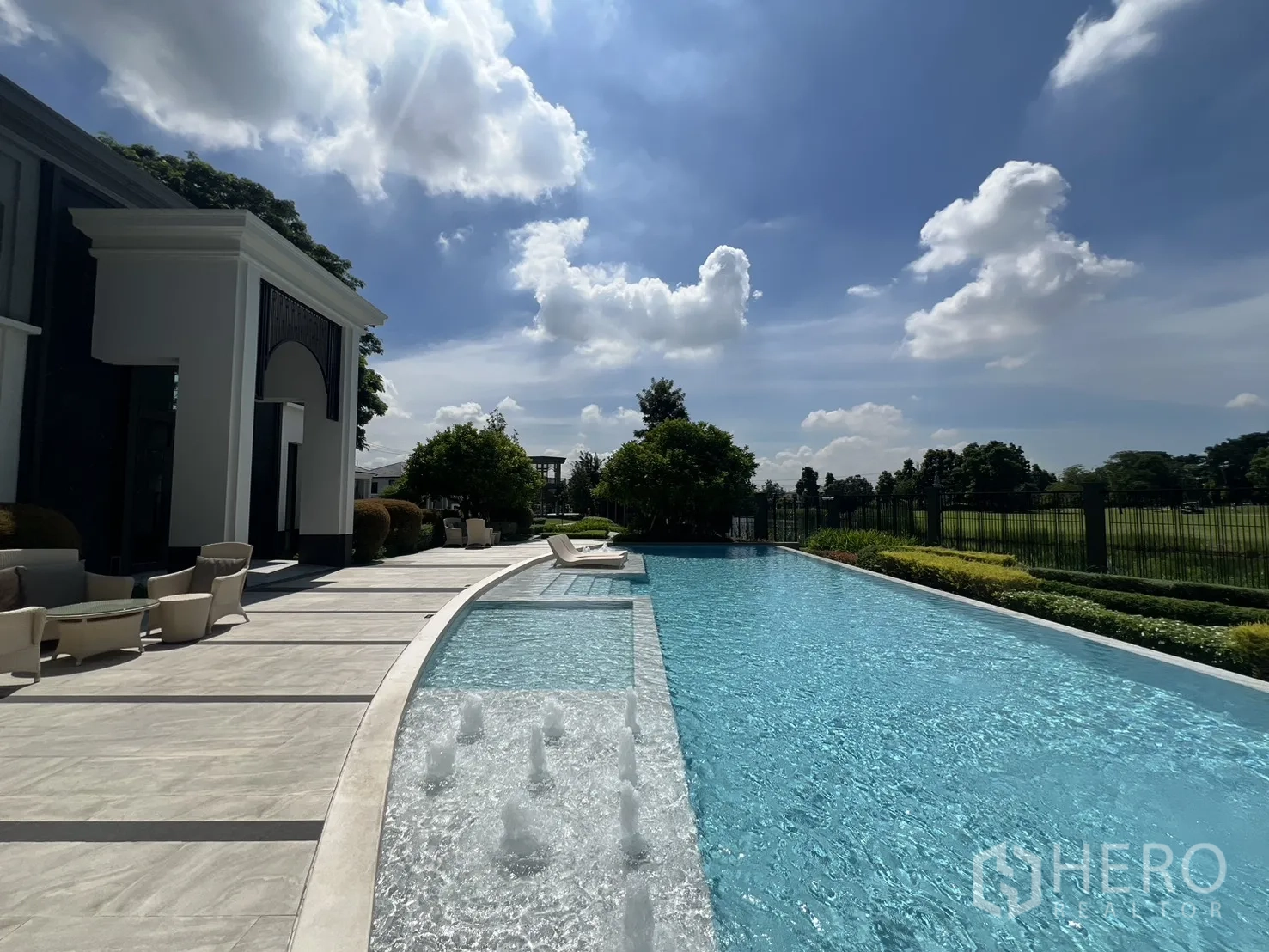 Detached House for rent or sale in Mueang Pathum Thani, Pathum Thani - Clubhouse facade beside an elongated swimming pool and seating terrace.