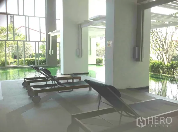 คอนโด ให้เช่าหรือขายในHuai Khwang, Bangkok - สระว่ายน้ำในร่มพร้อมเตียงพักผ่อนและกระจกสูงจรดเพดานมองออกสู่สวน