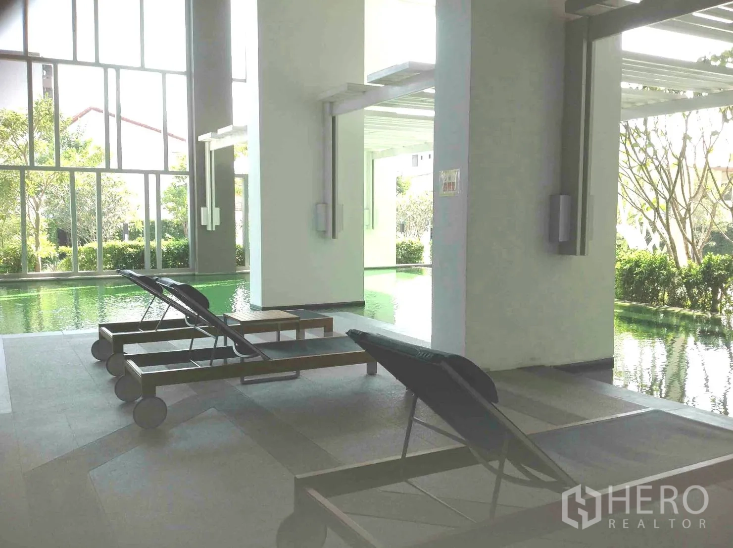 คอนโด ให้เช่าหรือขายในHuai Khwang, Bangkok - สระว่ายน้ำในร่มพร้อมเตียงพักผ่อนและกระจกสูงจรดเพดานมองออกสู่สวน