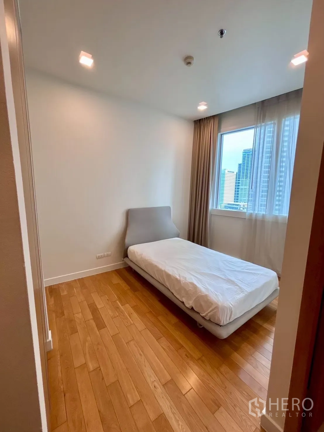 Condominium for rent in Khlong Toei, Bangkok - Cozy bedroom with single bed, wood flooring and city view