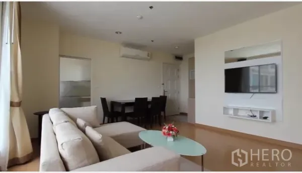 Condominium for rent in Watthana, Bangkok - Bright living room with cream sofa, glass coffee table, dining set and wall-mounted TV in a Bangkok condo.