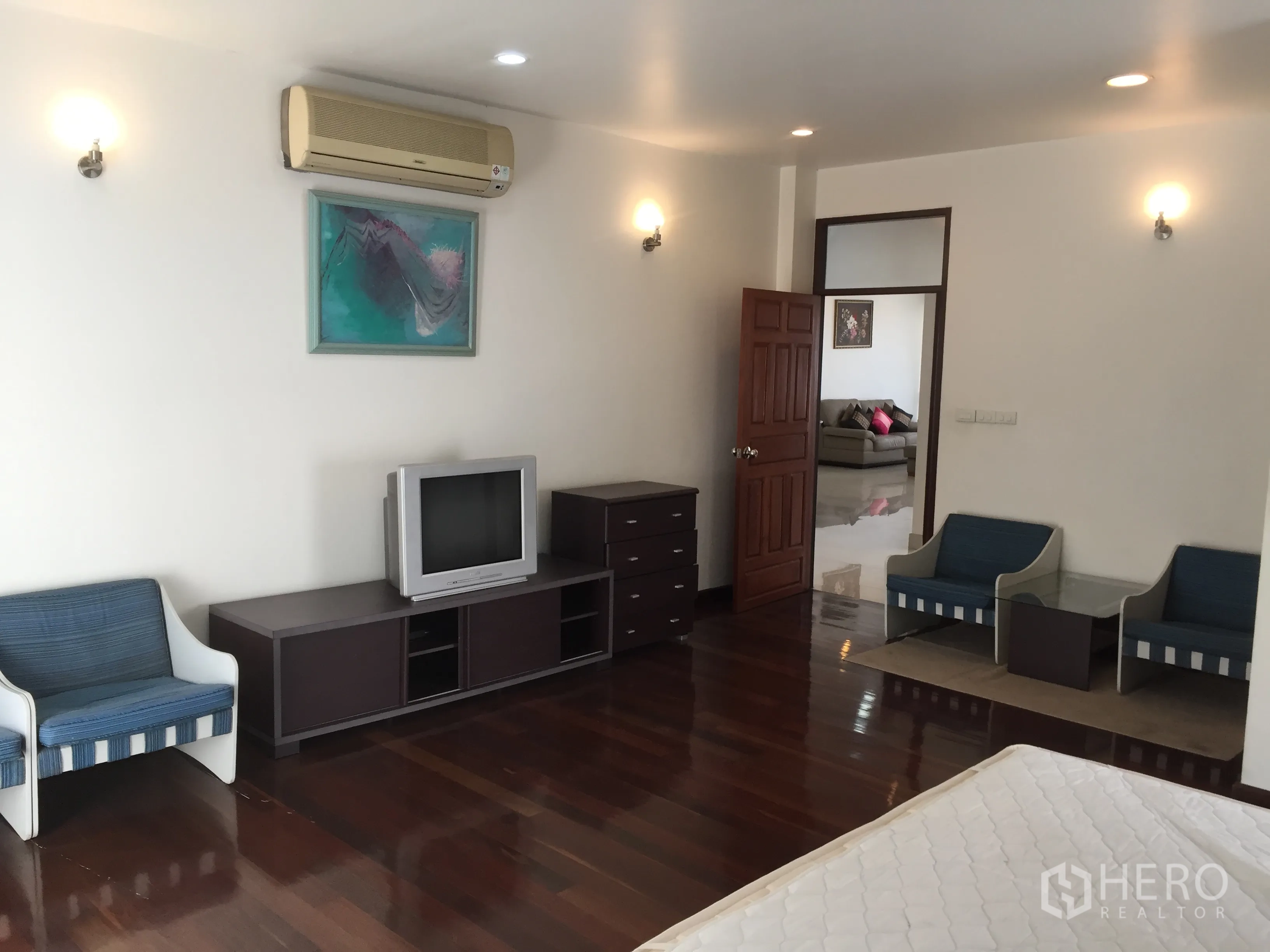 Condominium for rent in Watthana, Bangkok - Large bedroom with polished wood flooring, wall-mounted air conditioner, TV console and seating area.