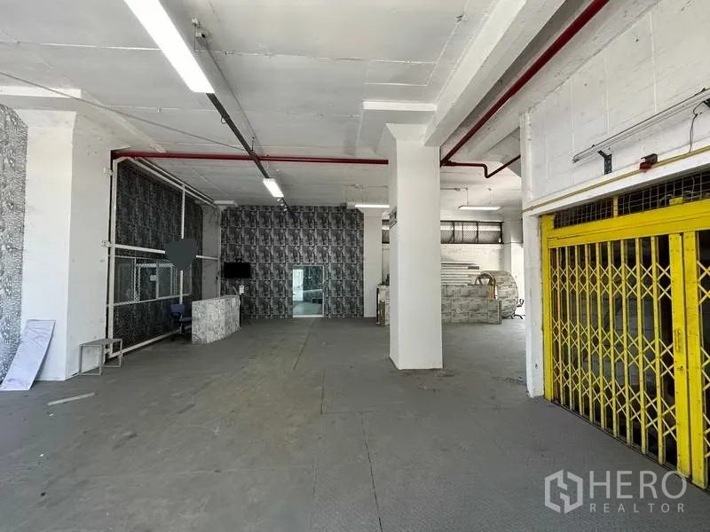 Factory for rent in Mueang Samut Prakan, Samut Prakan - Spacious factory hall with yellow folding gate, overhead lighting and red fire pipes.