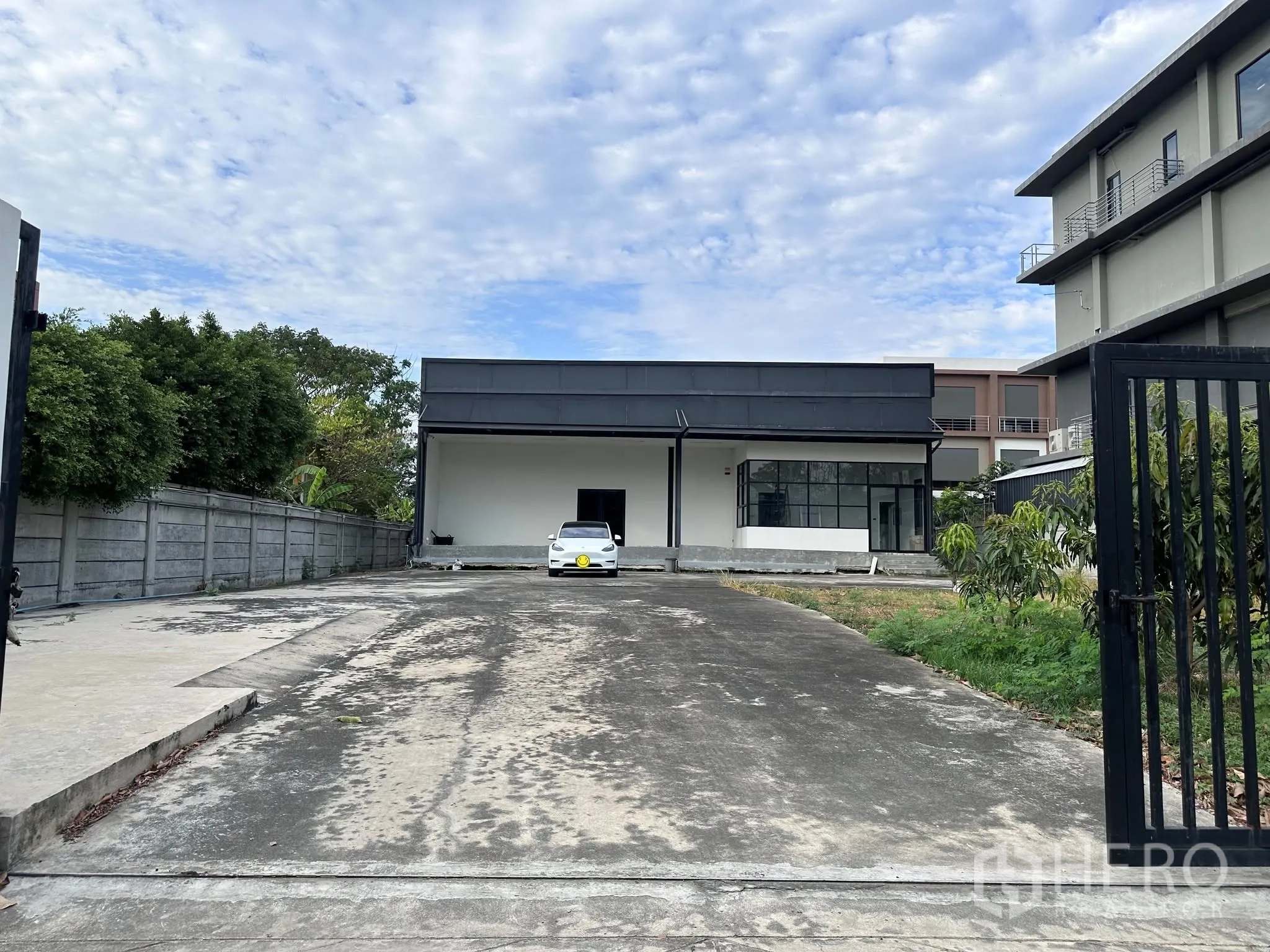 Warehouse for rent or sale in Prawet, Bangkok - Gated driveway leading to a single-storey warehouse with ample parking space.