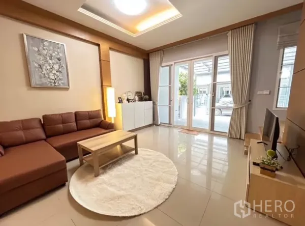 Townhouse for rent in Wang Thonglang, Bangkok - Bright living room with L-shaped leather sofa, TV console and sliding glass doors