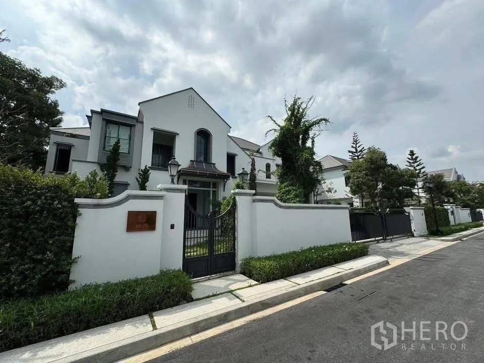 Detached House for sale in Taling Chan, Bangkok - Street view of a gated luxury housing estate with white perimeter wall and landscaped verge.