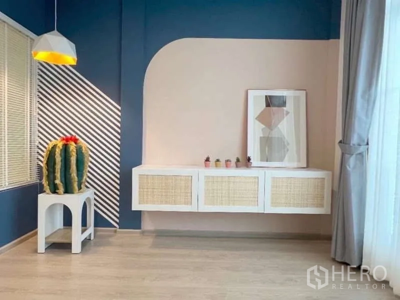 Townhouse for rent in Bang Bo, Samut Prakan - Stylish corner with navy and blush walls, pendant light, cactus on a side table and a floating rattan-front cabinet.