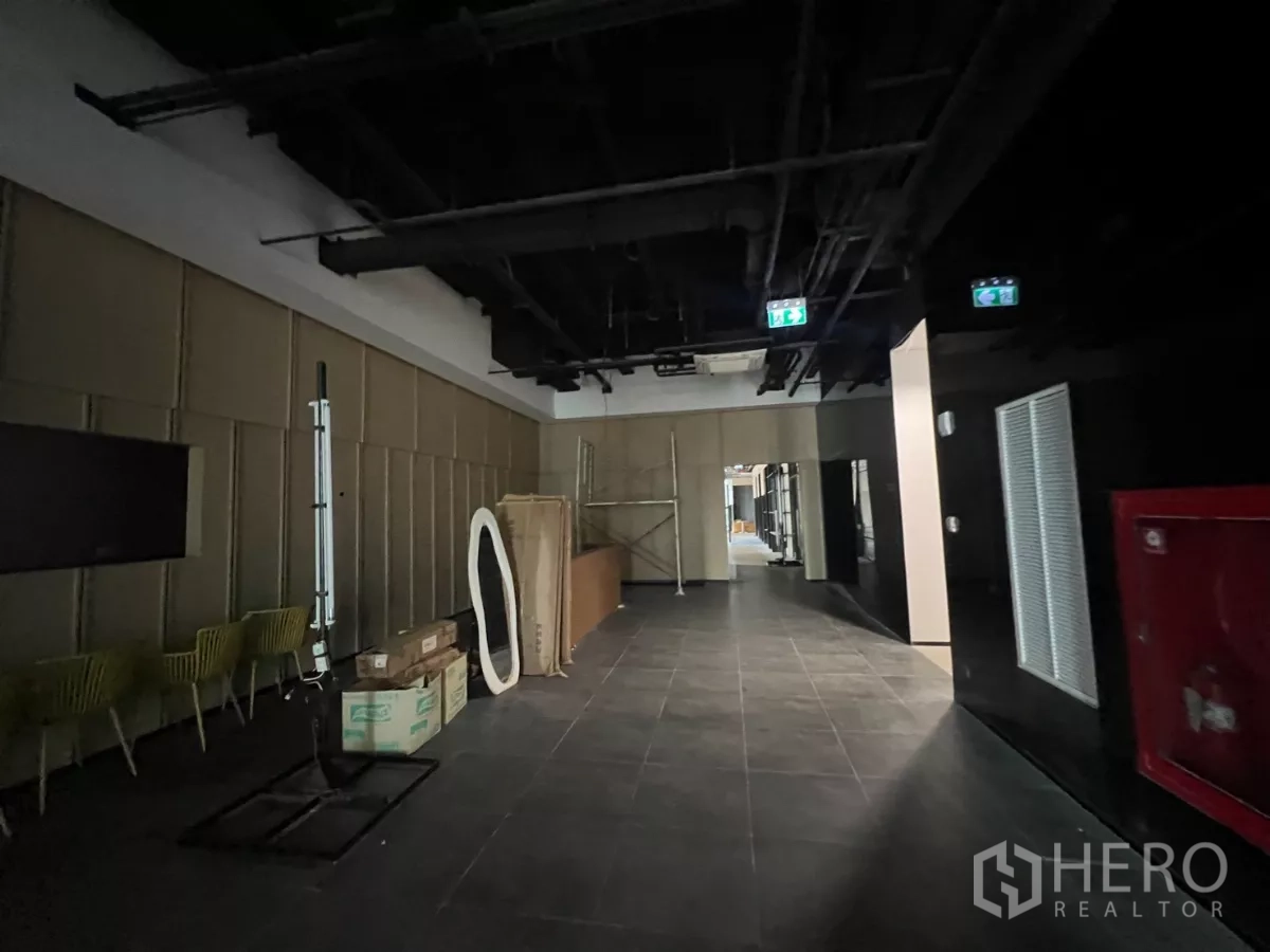 零售空间 出租 - 公共大堂区域，深色地砖、外露管线天花与紧急出口指示。