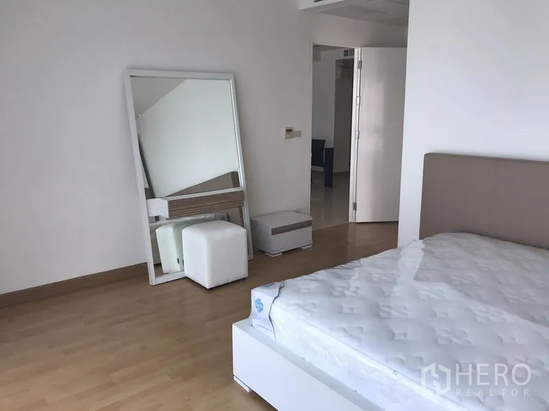 Condominium for rent in Khlong Toei, Bangkok - Second bedroom with bed, large standing mirror and bedside cabinet.