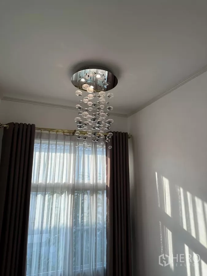 Detached House for rent or sale in Bang Phli, Samut Prakan - Modern crystal ceiling light above curtained window in the living area.