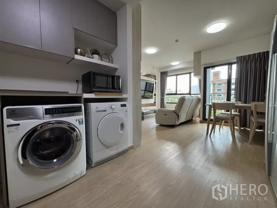 Condominium for rent in Phra Khanong, Bangkok - Open-plan space showing washer and dryer opposite the living and dining zones with wide windows.