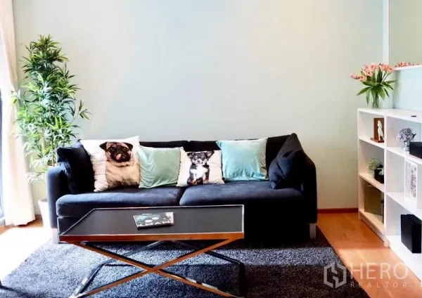 คอนโด ให้เช่าในWatthana, Bangkok - ห้องนั่งเล่นสว่าง โซฟาสีเข้ม ผนังพาสเทล โต๊ะกลางกระจก พรม ชั้นวางของ และต้นไม้ในบ้าน