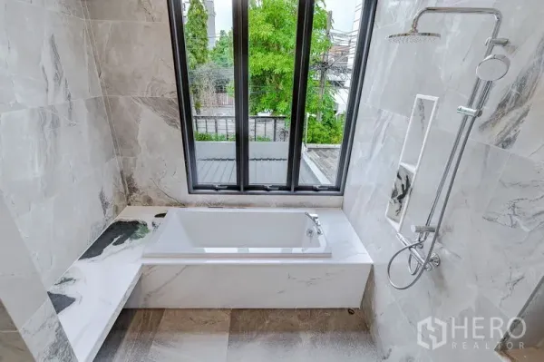 Townhouse for sale - Marble-tiled bathroom with soaking tub, rain shower, and tall windows overlooking greenery.