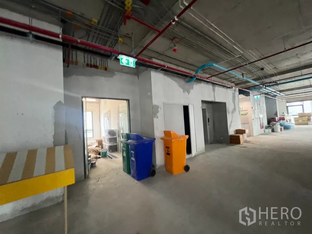 Office Space for rent in Khlong Toei, Bangkok - Core-and-shell office corridor showing exposed MEP lines, exit signage and service rooms.
