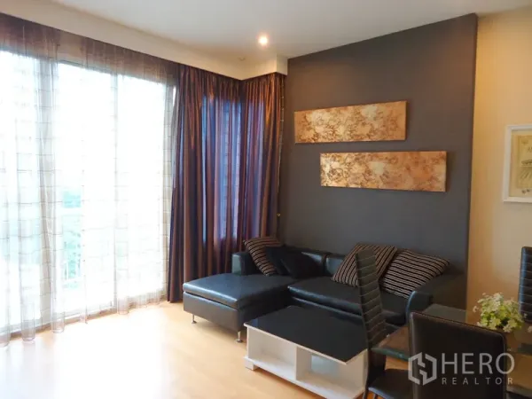 คอนโด ให้เช่าในChatuchak, Bangkok - ห้องนั่งเล่นมุมห้อง โซฟาหนังทรง L หน้าต่างสูงจรดเพดานและผ้าม่านทึบ