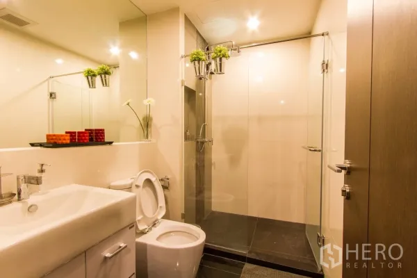 公寓 出租或出售在Sathon, Bangkok - 明亮浴室，超大镜面、洗手台、坐便器与玻璃淋浴间。