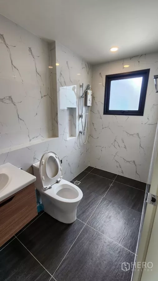 Detached House for rent in Bang Phli, Samut Prakan - Modern bathroom with marble-effect wall tiles, dark floor tiles, shower and toilet.