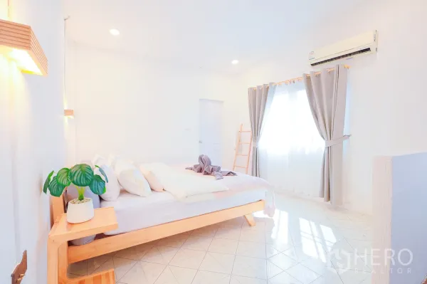 Townhouse for rent in Din Daeng, Bangkok - Minimalist bedroom with light wood bedframe, potted plant and large curtained windows.
