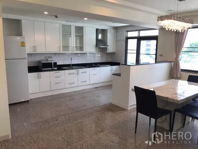 Condominium for rent in Watthana, Bangkok - Open-plan kitchen with white cabinets, black countertops and chandelier-lit dining.