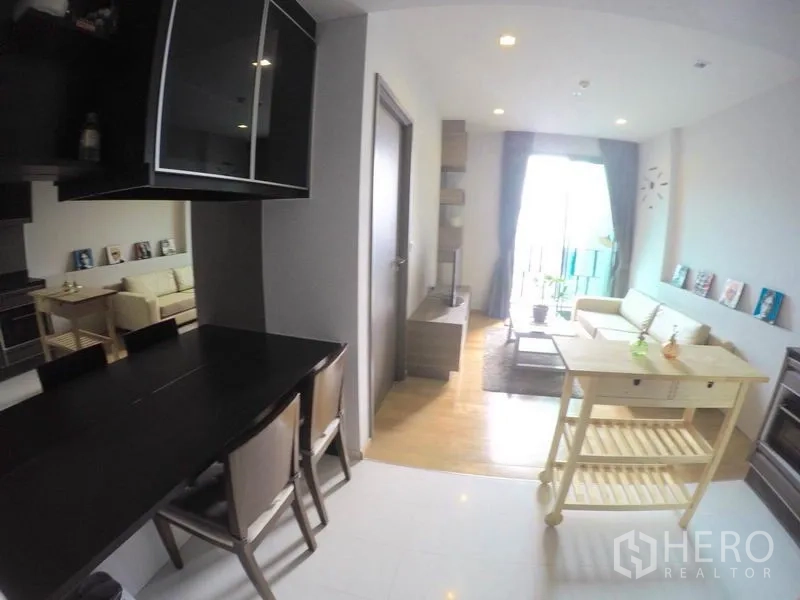 คอนโด ให้เช่าในKhlong Toei, Bangkok - โซนรับประทานอาหารและนั่งเล่นแบบเปิดโล่ง มีโต๊ะทานข้าวสีดำ รถเข็นเคาน์เตอร์ และประตูกระจกออกสู่ระเบียง