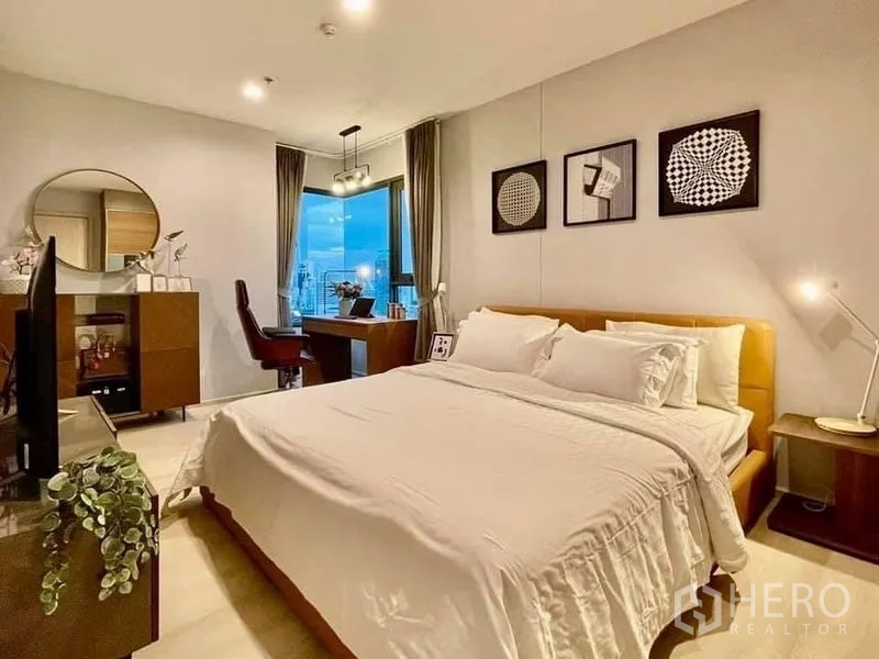 Condominium for rent in Pathum Wan, Bangkok - Spacious master bedroom with work area and warm lighting overlooking the city.