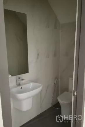 Factory for sale in Bang Bo, Samut Prakan - Clean restroom with wall-mounted sink, mirror, toilet and bidet spray.