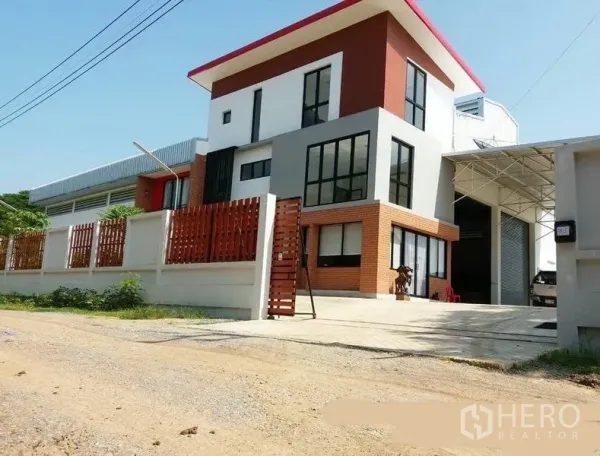Factory for rent or sale in Lat Lum Kaeo, Pathum Thani - Modern factory and office exterior with red roof, brick accents, gated driveway and wide roller door.