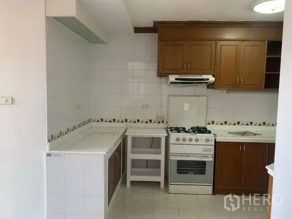 Condominium for rent in Watthana, Bangkok - Enclosed kitchen featuring wooden cabinets, white tiled walls, gas stove with hood and L-shaped countertop.