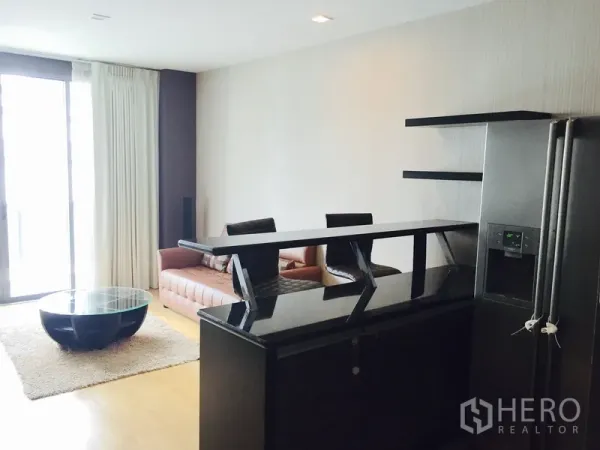 公寓 出租或出售在Khlong Toei, Bangkok - 起居区配吧台、沙发与大推拉玻璃门，旁有不锈钢冰箱。