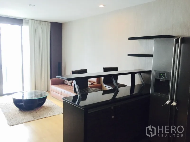 公寓 出租或出售在Khlong Toei, Bangkok - 起居区配吧台、沙发与大推拉玻璃门，旁有不锈钢冰箱。